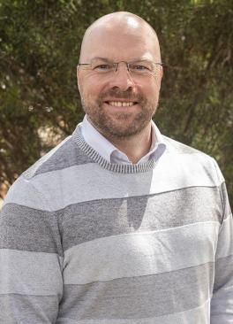 Bald man with striped jumper and glasses and beard in front of a tree