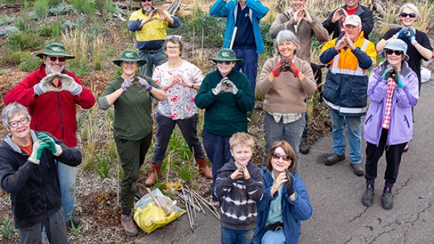 Photo of a group of people standing on a tree planting site, looking at teh camera and making the Landcare sign with their hands