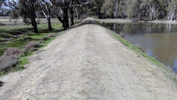 n earthen levee with trees and a paddock on the left side and a river on the right