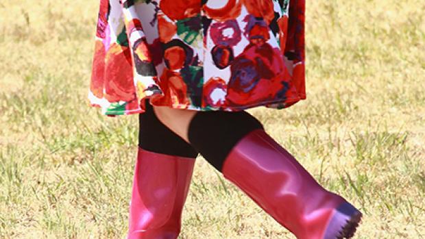 Photo of a woman from teh waist down wearing a red dress and red gumboots, walking in a field