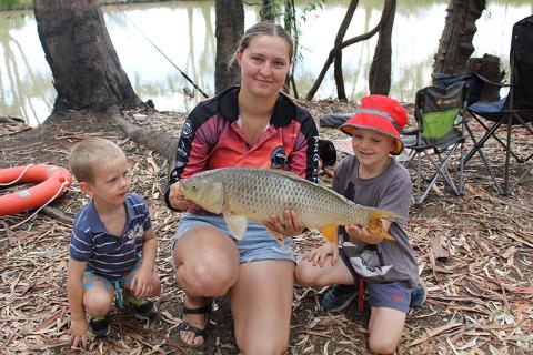Teenage girl holding a carp in front of river with two small boys either side of her.