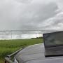 Laptop sits on a grey car bonnet in the foreground. Is the background is an irrigation sprayer over a green crop