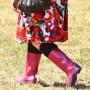 Photo of a woman from teh waist down wearing a red dress and red gumboots, walking in a field